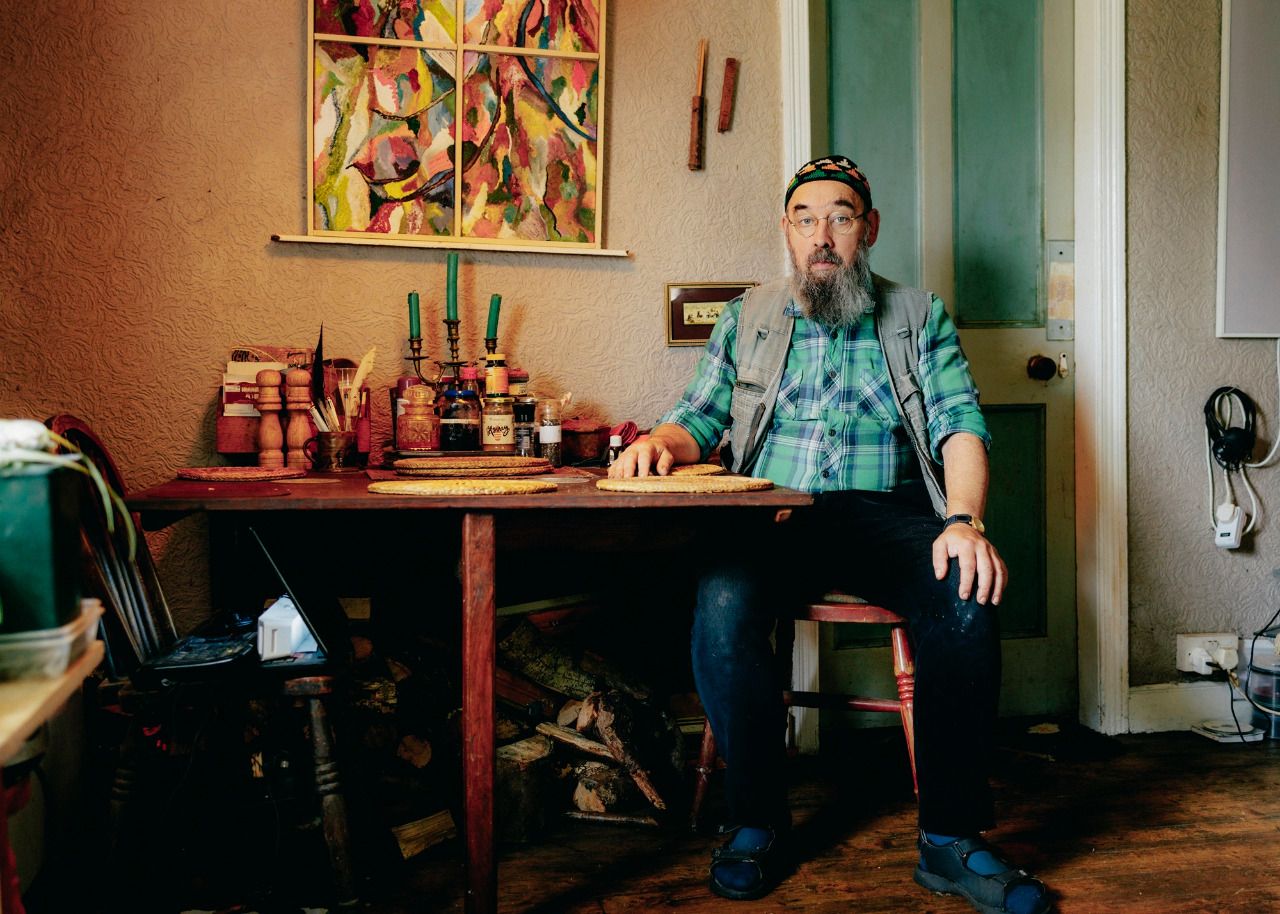 Malcom sitting at his kitchen table surrounded by household clutter